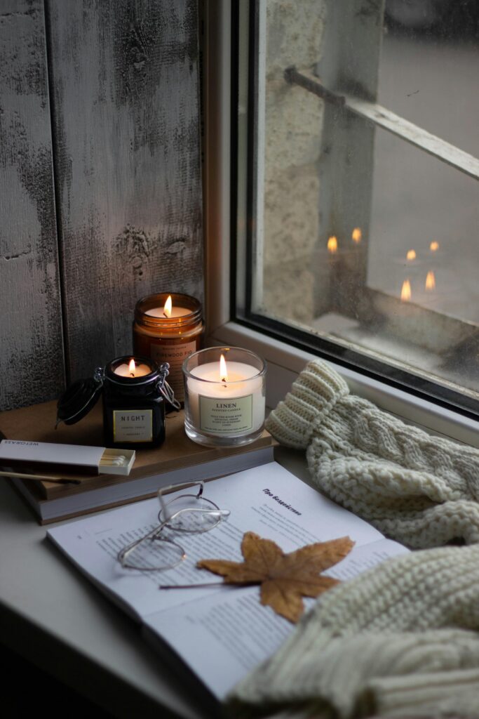 A hygge-inspired scene with candles, books, and autumn leaves by a window, perfect for fall ambiance.