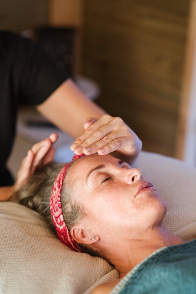 Crop masseuse giving massage reiki while standing near with hands near head of client in comfortable spa on blurred background